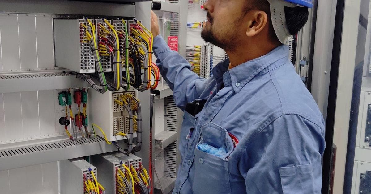 Teknisi K3 listrik berhelm memeriksa kabel di panel kontrol listrik industri