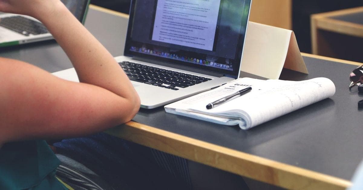 Laptop terbuka dan buku catatan di meja peserta kelas daring