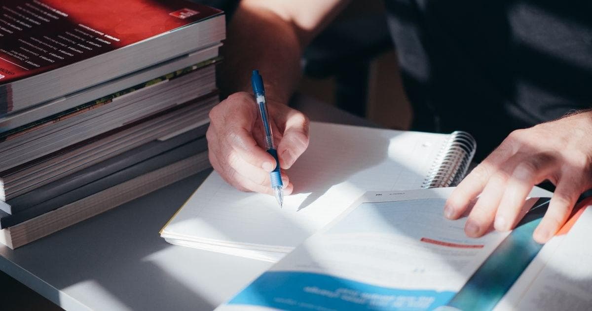 Peserta menulis catatan belajar di samping tumpukan buku materi ujian